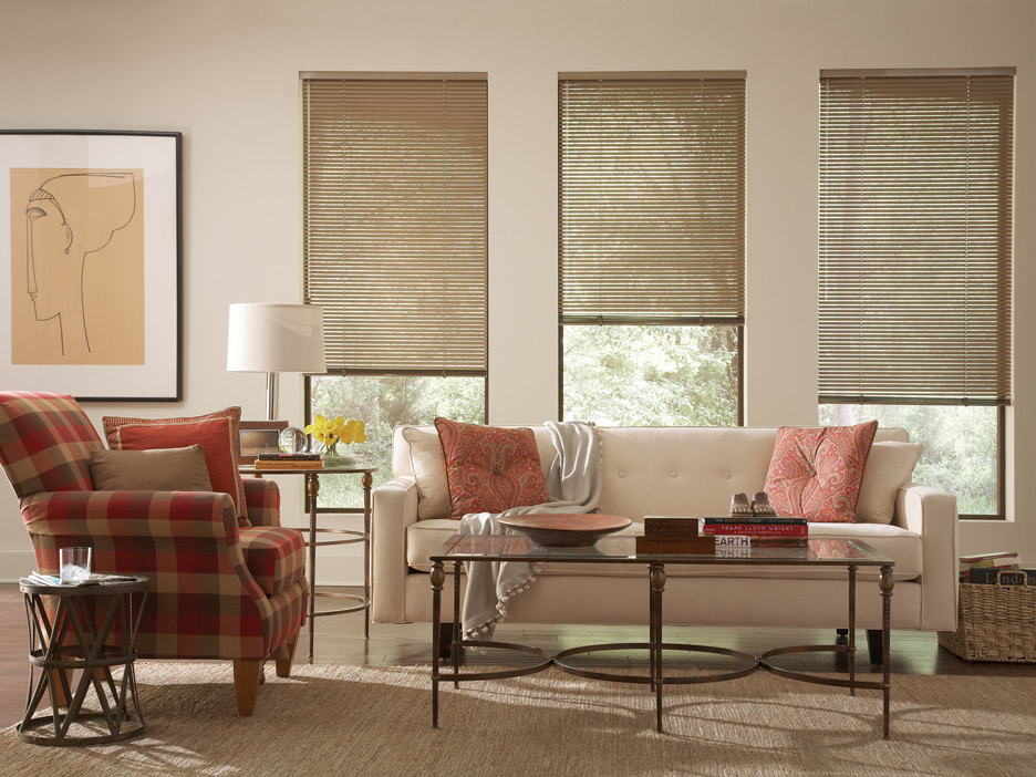 Brown Classic Collection® Aluminum Blinds against white walls with light red Interior Masterpeices® Custom Pillows on a cream colored couch with a red plaid chair off to the side