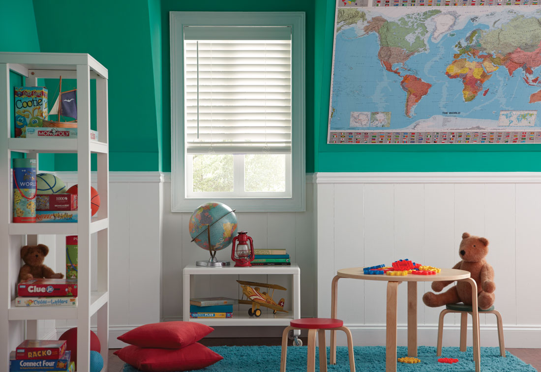 White Heartland Woods® Wood Blind against a green wall in a kid's room with a globe and other toys laying about