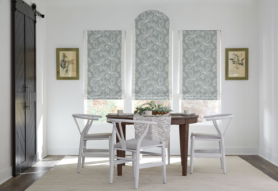 Three light blue floral patterned Interior Masterpieces® fabric shades with a custom arch top in the middle behind a brown table with white chairs