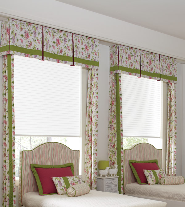 bedroom with two beds that have windows behind them with Parasol® cellular shades and custom Interior Masterpieces® cornices, draperies, and pillows that match in a light floral pattern