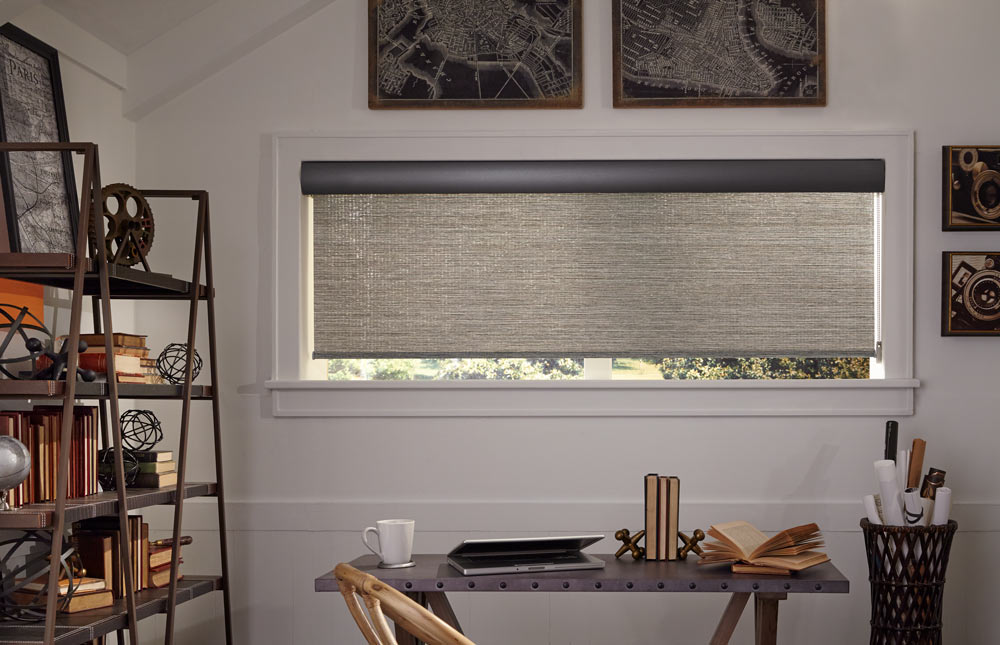 wide brown Genesis® Roller Shade with a dark Cassette in an office behind a metalic desk and brown chairs