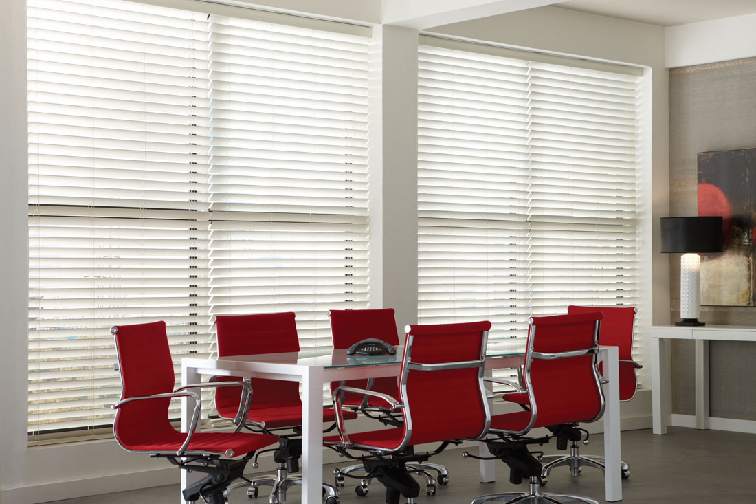 Large white Wonderwood® Wood Blinds in an office with red chairs and a metal table