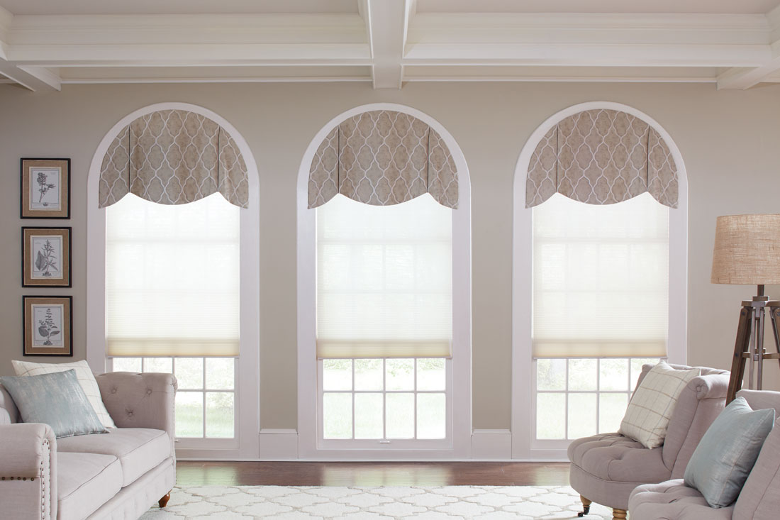 Three light colored Parasol® Cellular shades in windows with rounded tops that have custom Interior Masterpieces® Cornices on top