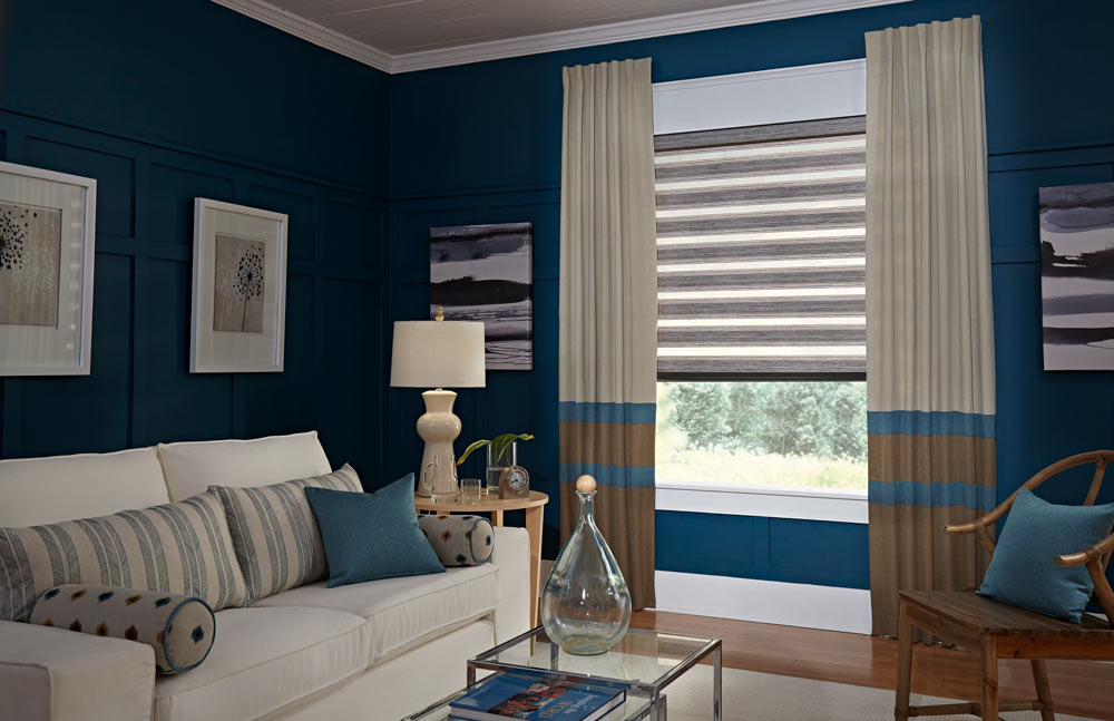 brown Allure® Transitional Shade against a dark blue wall with tan, brown, and blue striped Interior Masterpieces® Draperies behind a couch with matching custom Pillows