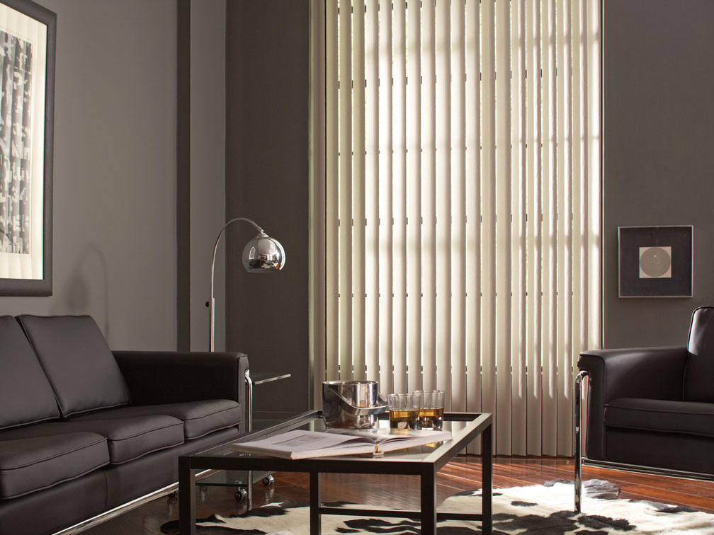 White Discoveries® Vertical Blinds in a room with gray walls and black furniture