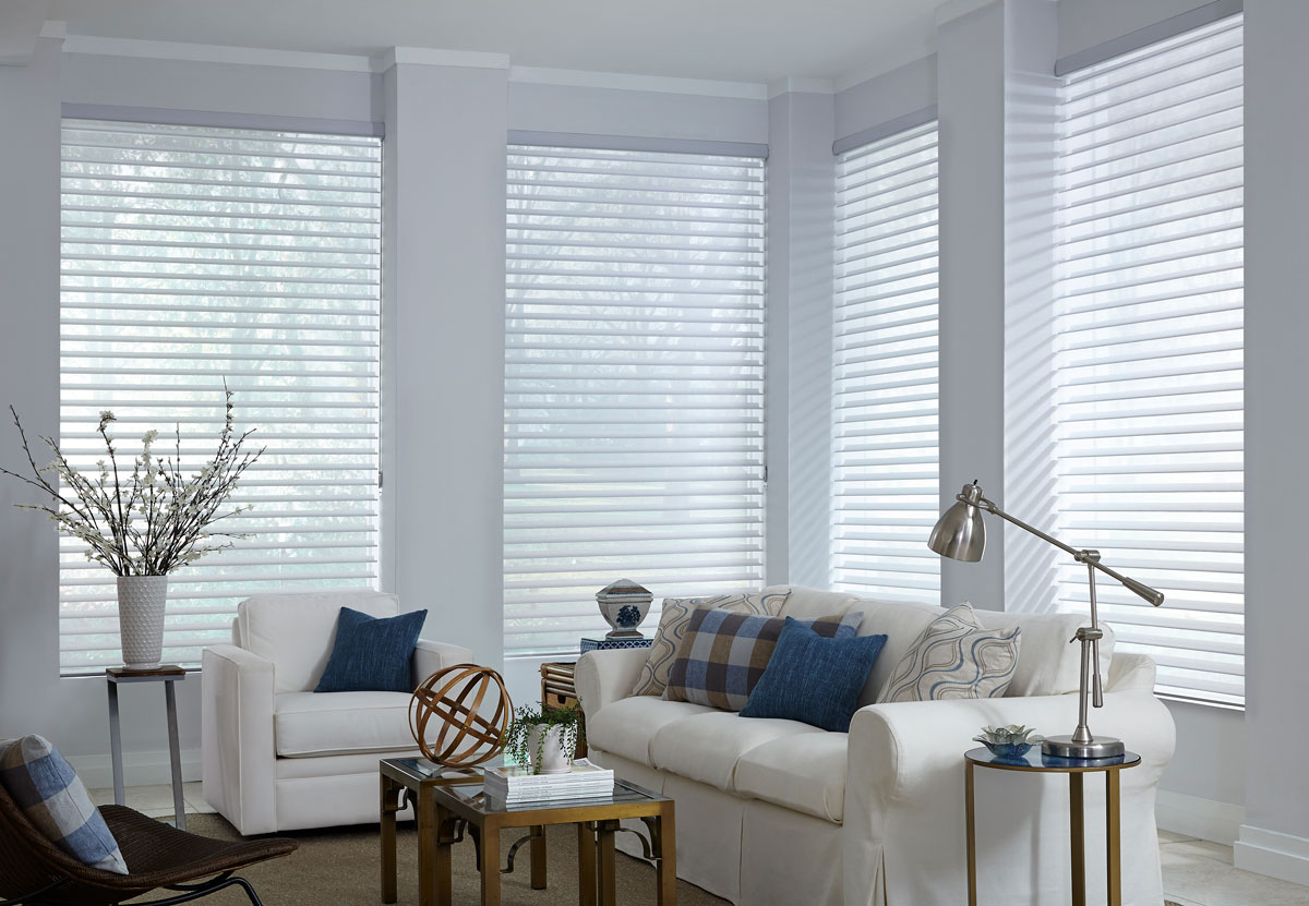  Several white Tenera® Sheer Shades in the open position in a room with white walls and a white couch with a white chair that have blue and blue plaid Interior Masterpieces® custom pillows 