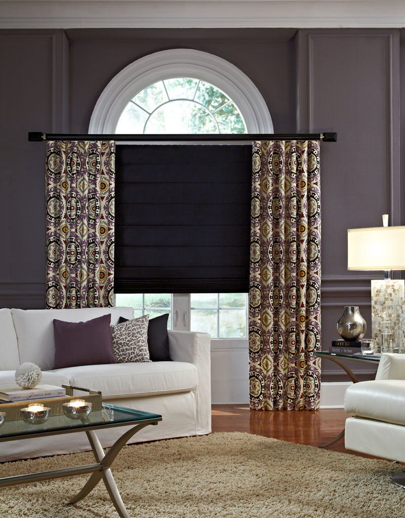 hobbled black Interior Masterpieces® fabric shade with tan and black geometric pattern draperies hanging at each end on a dark custom rod with wide finials