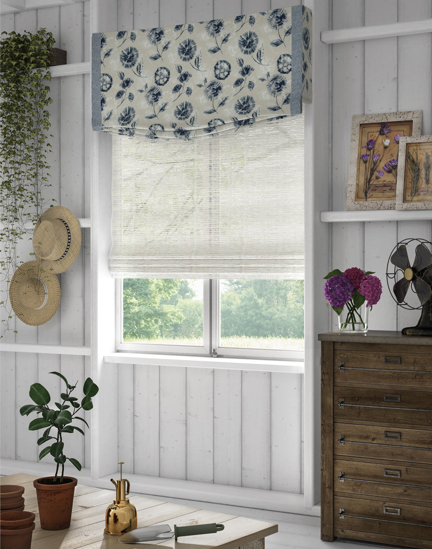 a white Manh Truc® Woven Wood Shade with a light white and blue floral patterned Interior Masterpieces® Fabric Valance with light blue Decorative Banding in a shed with gardening tools around