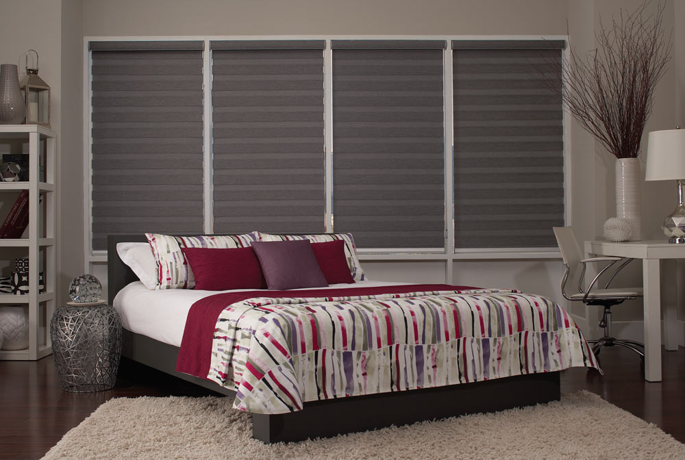 four large dark gray Allure® Transitional Shades against a beige wall behind a bed with Interior Masterpieces® Custom Bedding in maroon, purple and white with an erratic striped pattern