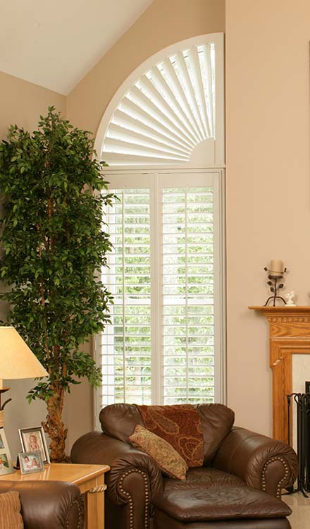 off white Parke® Shutters with a Quarter Circle Custom Shape and a tall potted plant in the foreground and a brown chair