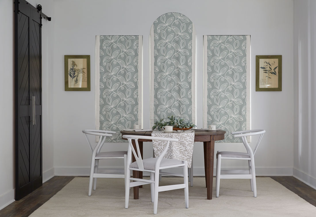 Three light blue floral patterned Interior Masterpieces® fabric shades with a custom arch top in the middle behind a brown table with white chairs