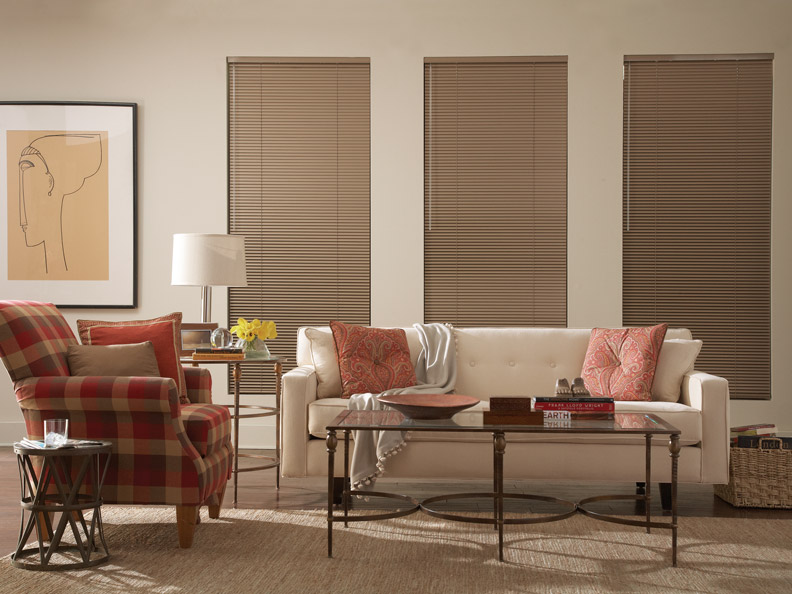 Brown Classic Collection® Aluminum Blinds on a cream colored wall with light red floral Interior Masterpeices® Custom Pillows on a light couch with a red plaid chair off to the side