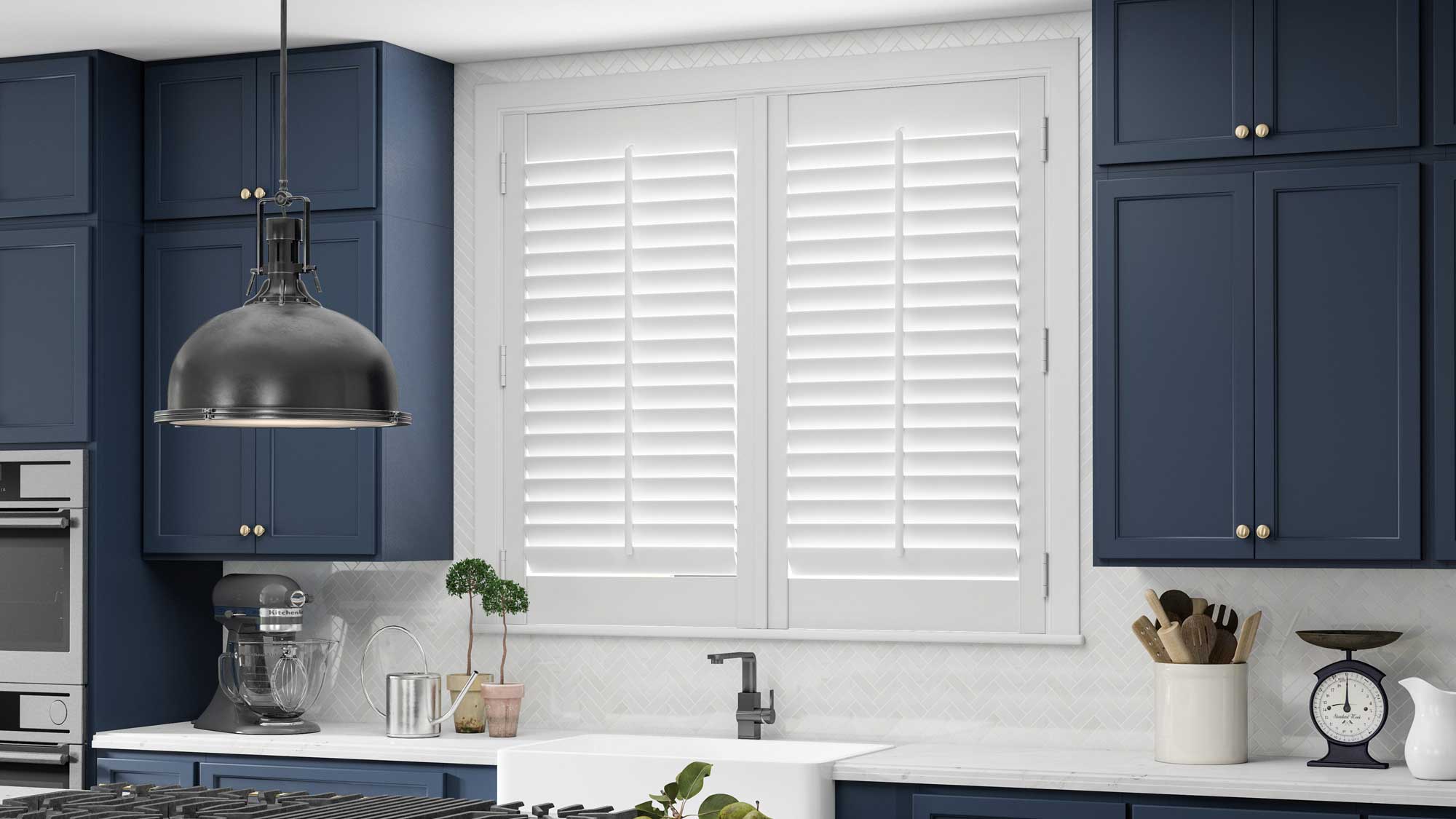 white Parke® Shutters in a kitchen with blue cabinets, a sink, and an island stove top with marble counters in the foreground