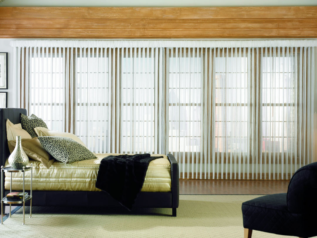 One very large Sheer Visions® Vertical Blind over a wall of windows in a bedroom with a bed and custom pillows on it
