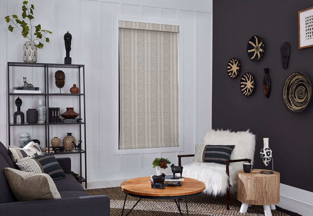 Tan and black patterened Interior Masterpieces® fabric shade with matching fabric cornice in a room with a fluffy chair and couch with accenting custom pillows