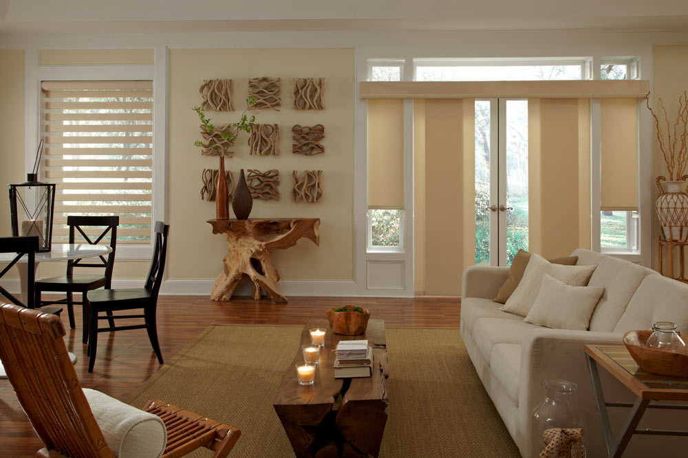 beige colored Allure® Transitional Shade in a window beside a large patio door with the same colored Genesis® Companions Panel Track behind a tan couch with pillows