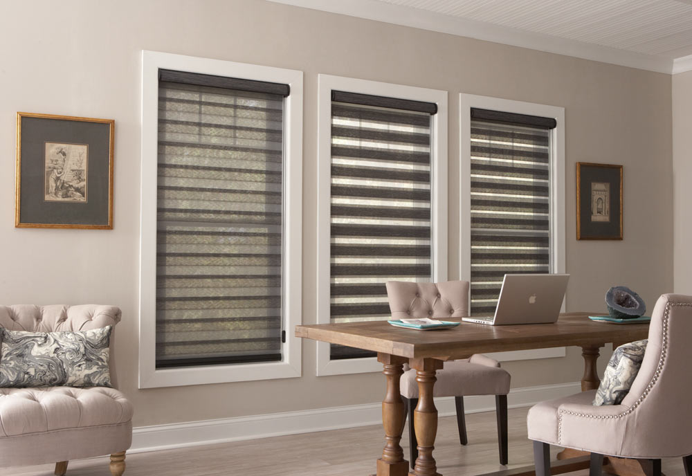 three large dark gray Allure® Transitional Shades on a beige wall behind a table with a laptop on it