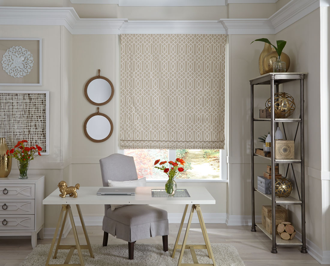 patterned tan Interior Masterpieces® fabric shade in a window behind a desk with a gray chair and laptop