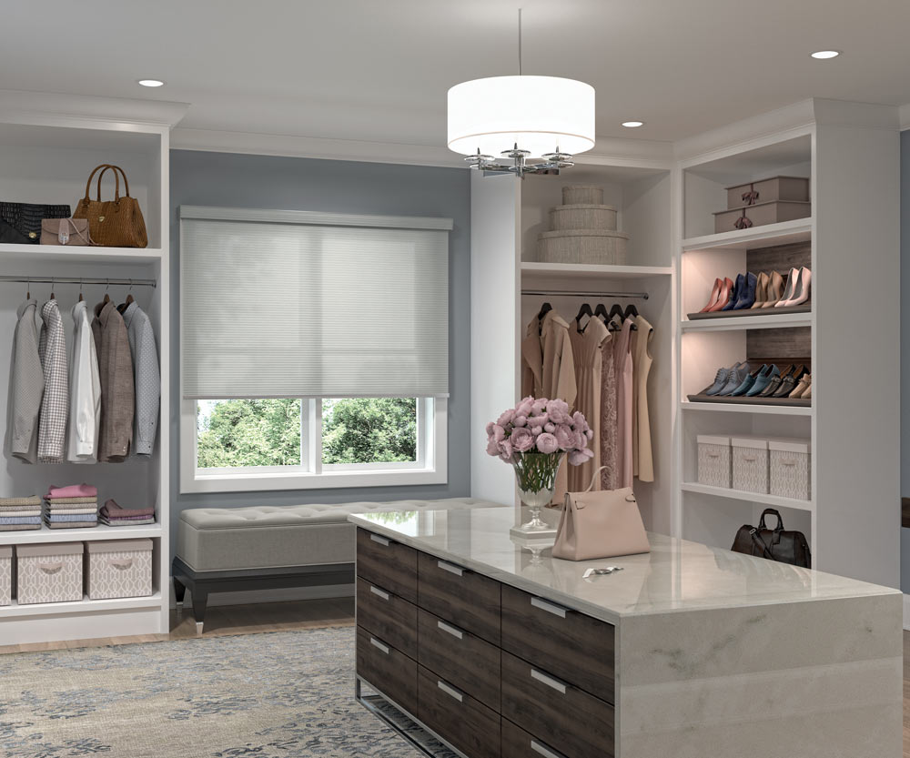 large gray Genesis® Cassette Roller Shade in a closet next to clothes and a dresser in the foreground with pink flowers on it