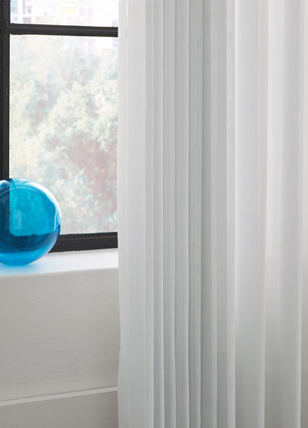 Close up shot of white sheer fabric vertical wrapped blinds show the uniform folds when drawn open.