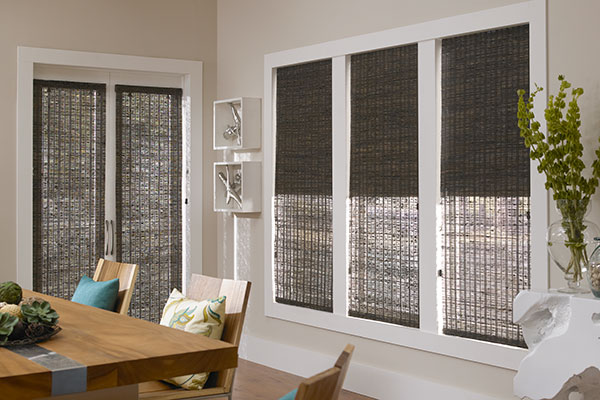 Three dark brown woven wood shades hang in three windows to show the difference in opacity of unlined, lightly lined, and room darkening lined shades.