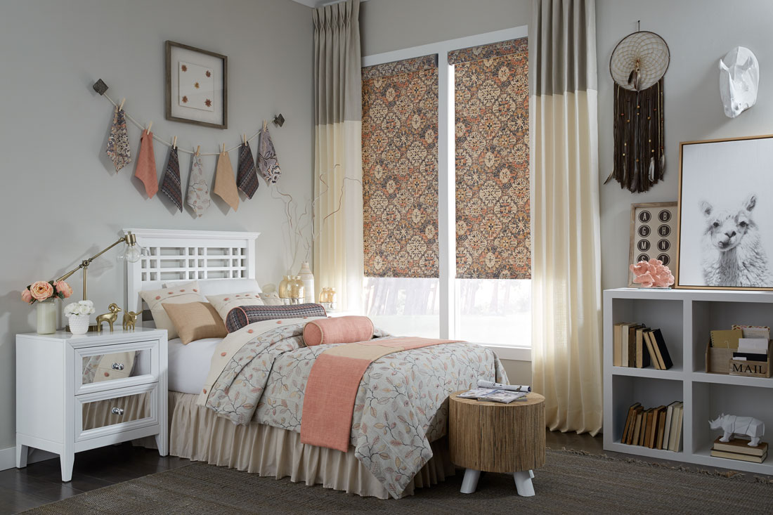 Geometric floral patterned orange and brown Interior Masterpieces® fabric shades with gray and tan draperies hanging on each side with custom bedding on the bed in front