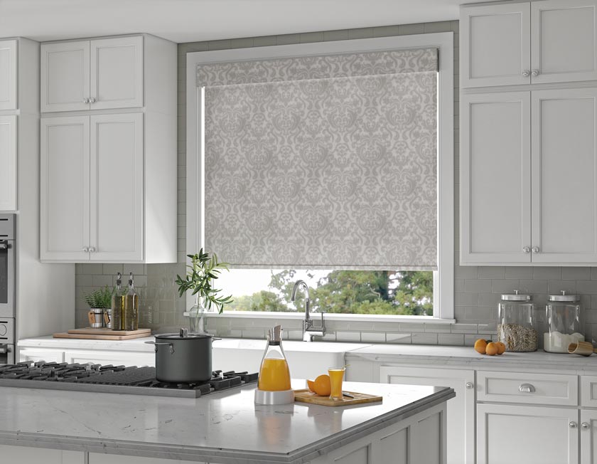 Gray patterened Genesis® Roller Shade with Cassette in a kitchen with gray walls and white cabinets with an island stove top in the foreground