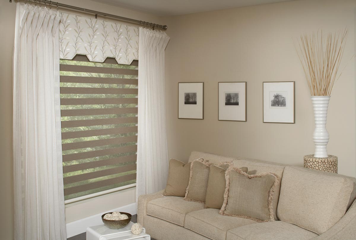 Tan room with white Interior Masterpieces® draperies hanging around a custom Fabric Wrapped Cornice and an Allure® transitional shade