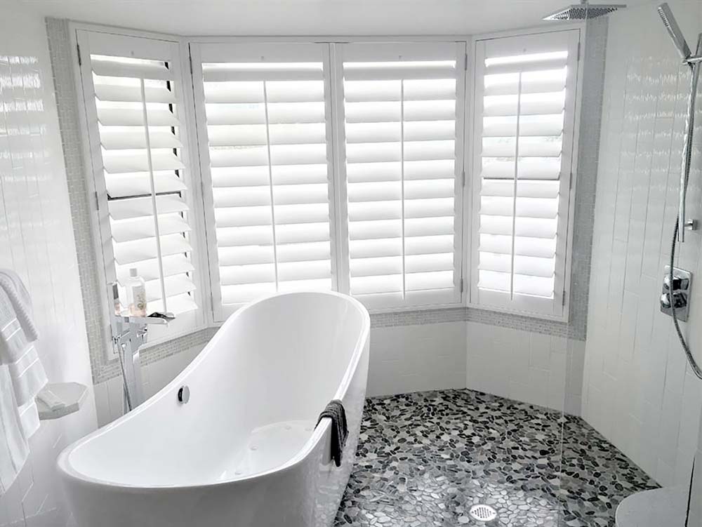 several white Parke® Shuttersin a bathroom with a bath tub in front