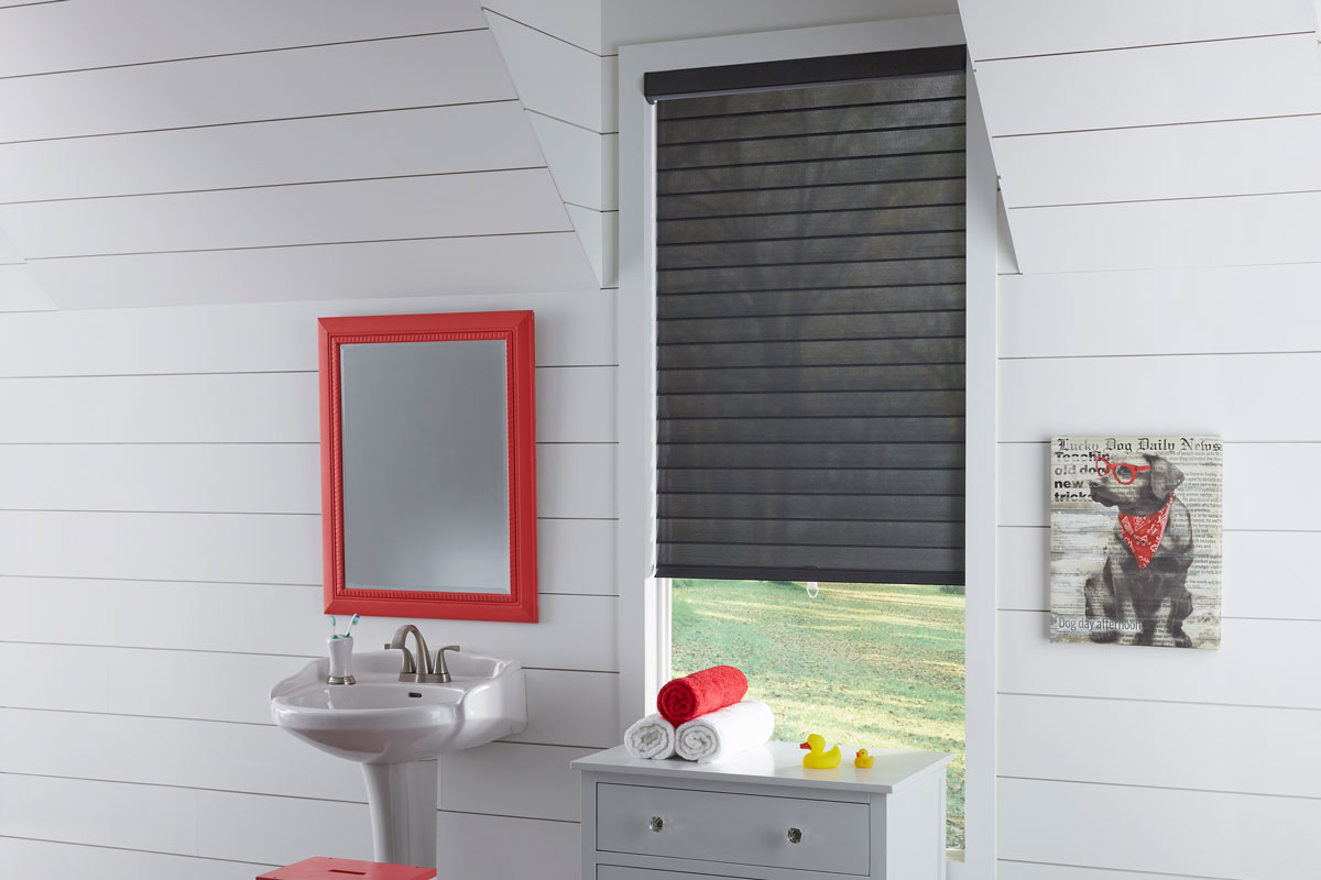 A black Tenera® Sheer Shade with vanes open in a white bathroom with a sink and red mirror next to it