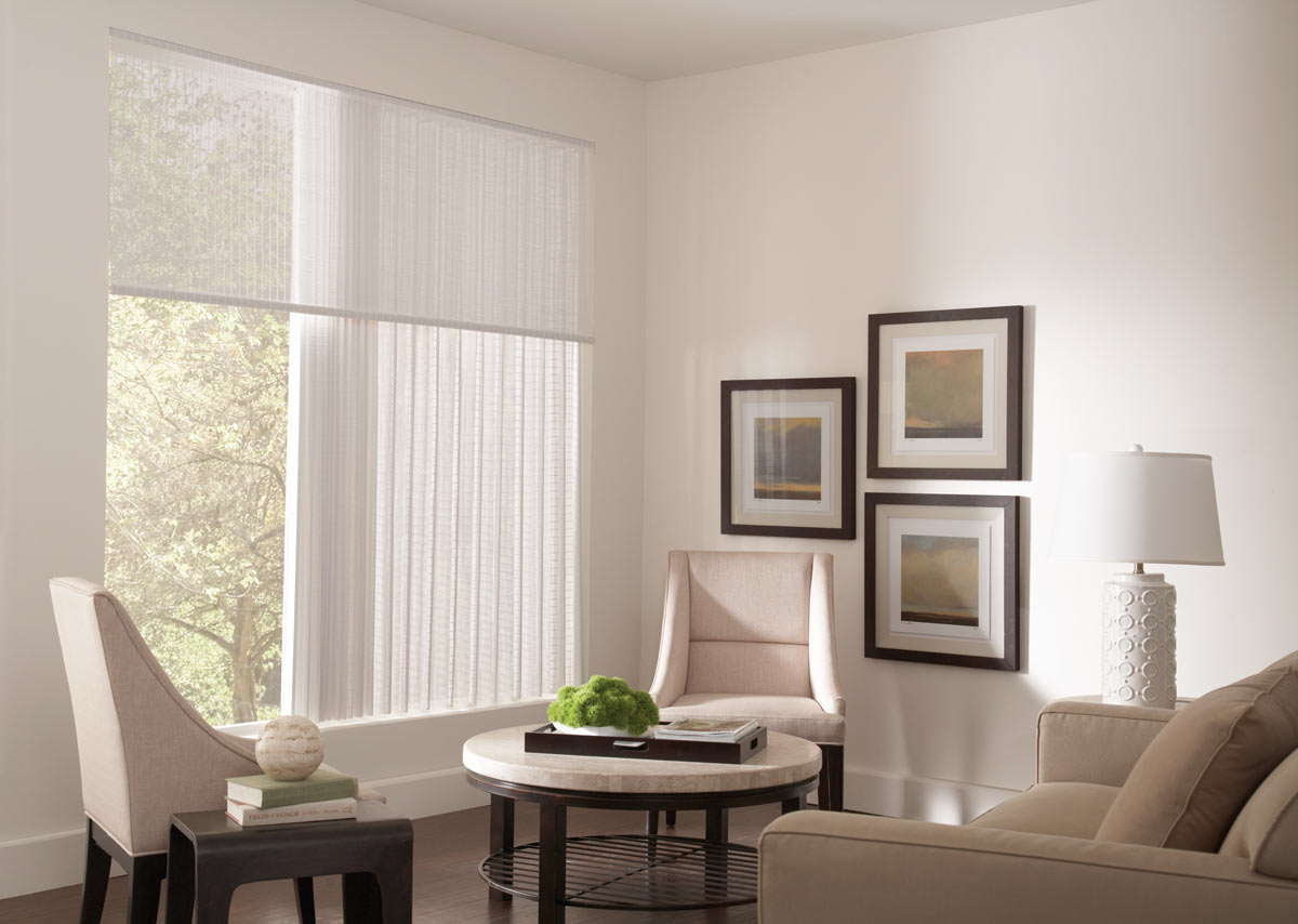 A large, closed white Manh Truc® Woven Wood Panel Drape in a picture window with a Valance in the same material next to a tan table and chairs