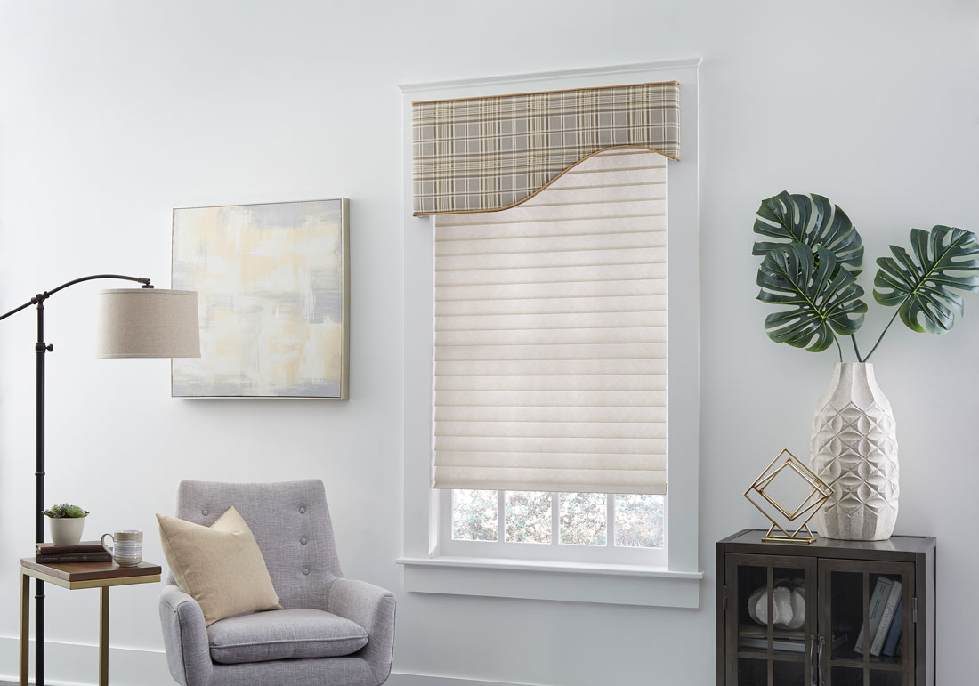 Light brown Tenera® Sheer Shade with light brown plaid Interior Masterpieces® Fabric Wrapped Cornice in a white room with a chair that has a custom Interior Masterpiece® pillow