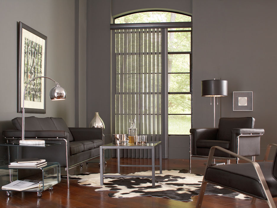 Gray Discoveries® vertical blinds hanging in a window in a room with gray walls and black furniture
