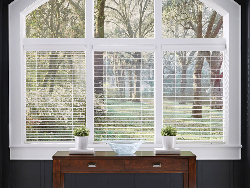 Three custom white wood blinds in three slat sizes, tilted open, hang in an arched window