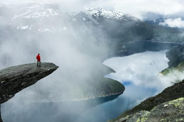 man-sits-end-trolltunga-before-mountains