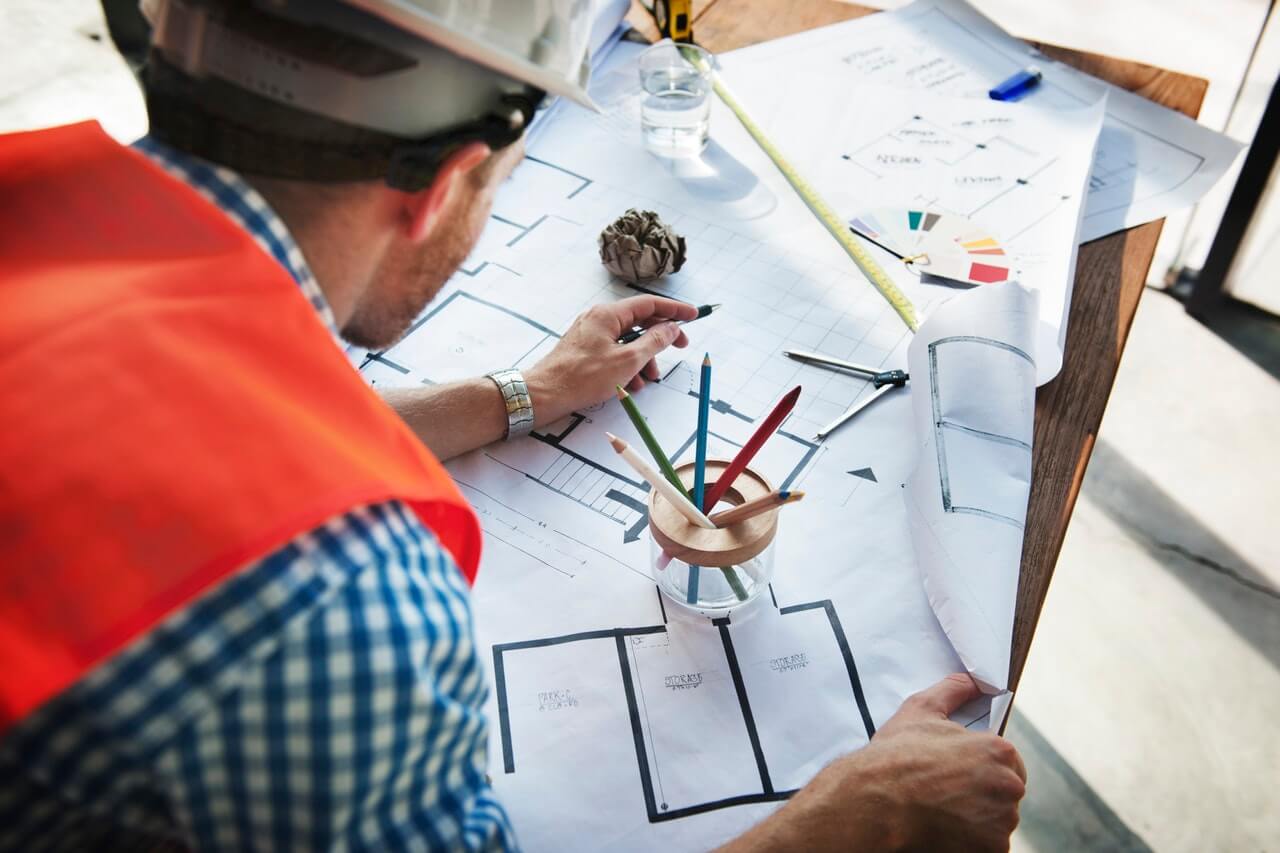 Man in Hard Hat working on building plans, budget adherence and schedule