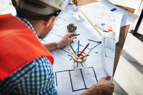 Man in Hard Hat working on building plans, budget adherence and schedule