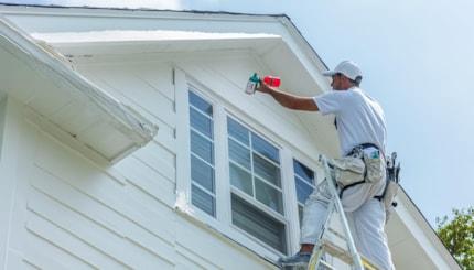 painter-professionally-painting-house-exterior-white-balancing-ladder-against-window-with-blue